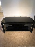 Front view of black TV stand showing metal frame and three black glass shelves.