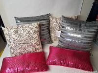 Top down view of 6 decorative throw pillows showing two ivory beaded, two grey sequined, and two hot pink sequined rectangular pillows.