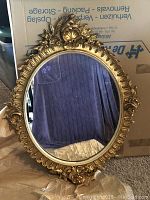 Full view of the oval mirror showing gilded plaster and wood frame with floral and shell decoration.