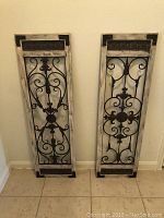 Full view of the pair of rustic wood framed wall hangings with black decorative metal scrollwork and distressed whitewash finish.