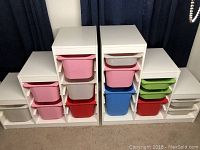 Full view of two white Trofast shelving units with various colored bins placed inside compartments.