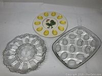 Three egg/oyster dishes: round scalloped glass, rectangular glass with oval indentations, ceramic with yellow divots and rooster design