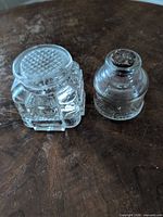 Octagonal pressed glass inkwell and cylindrical molded glass inkwell with cork on wooden surface