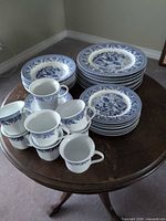 Stacked blue and white dinner, soup/dessert plates and matching mugs on round table