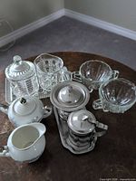All four cream and sugar sets: porcelain floral, stainless steel on tray, pressed glass set on tray, ribbed clear glass set