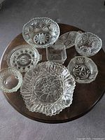 All eight clear pressed glass and crystal serving pieces displayed on round wooden table