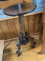 Full view of solid wood plant stand showing round top, turned column, and scroll-cut tripod base