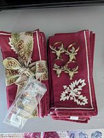 Stacked burgundy embroidered napkins, ribbon tied, with four brass deer head napkin rings and boxed bottle stopper