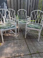 Set of four white faux bamboo armchairs with green leaf cushions on patio