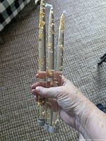 Hand holding three gold-foil lucite candles showing length, foil pattern, ribbed bases