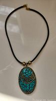 Front view showing turquoise mosaic and brass spiral design on oval pendant attached to black cord