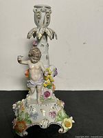 Full view of porcelain candlestick front showing cherub, applied flowers, gilt accents