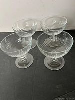 Four clear Quadro pattern footed dessert bowls aligned on black surface