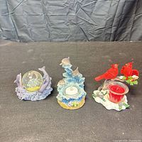Front view of all three resin pieces: dolphin snow globe, dolphin tealight holder, cardinal candle holder