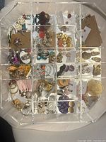 Overall view of acrylic box open showing assorted earrings and rings in compartments