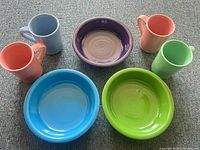 Group shot of all seven Fiesta pieces: three bowls (blue, green, purple) and four mugs (light blue, coral, lavender, green)
