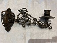 Full view of bronze wall sconce showing backplate, articulated arm, drip pan, candle cup