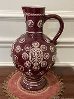 Full left-side view of the burgundy stoneware pitcher showing overall form and decoration