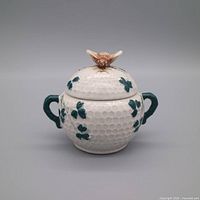 Front view of ceramic sugar bowl showing honeycomb body, clover leaves, handles, and bird finial