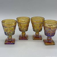 Front view of all four amber carnival glass goblets with square bases
