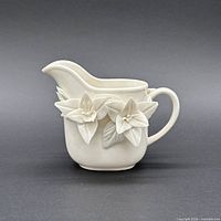 Front view of cream porcelain creamer showing applied floral motifs and handle