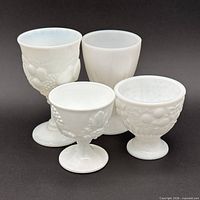 Front view of four milk glass goblets displaying patterns and shapes