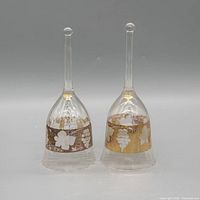 Front view of both clear glass bells showing grapevine gilt bands and handle shape