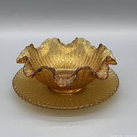 top view of ruffled amber carnival glass bowl on underplate