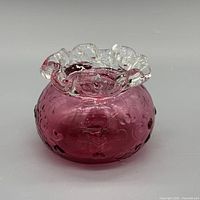 Front view showing cranberry glass body, clear ruffled rim, embossed pattern