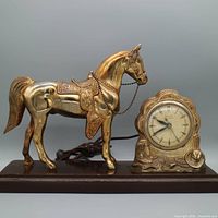 Full view of gilded horse clock on wooden base with cord