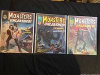 Three bagged Monsters Unleashed comics laid out on black surface
