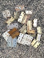 Group of assorted brass, nickel, painted and raw steel door hinges spread on gravel