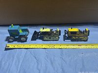 Three vintage toy bulldozers lined up with tape measure