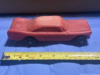 side view of red hard plastic toy car with tape measure showing length around 8.5 in