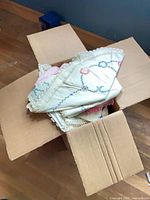 Box containing folded embroidered linens with lace trim