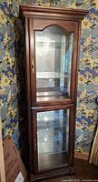 Front view of tall dark wood curio cabinet with glass shelves