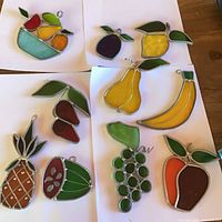 Group view of all ten stained glass fruit suncatchers laid out on white paper