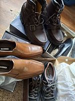 Overview showing four pairs of shoes: tan loafers, brown boots, black loafers, grey sneakers in boxes