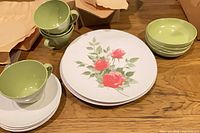 Stacked dinner plates with rose motif, green cups and bowls nearby