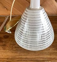 Conical white and clear striped glass shade with brass canopy and wiring visible