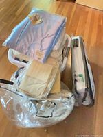 Stack of packaged bedding in bin including blue satin pillow cover, lace duvet cover, fitted sheet, sealed coverlet set