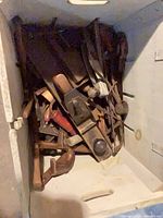 Assorted vintage hand tools piled inside wooden box