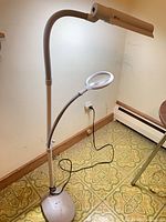 Full view of OttLite floor lamp showing lamp head, flexible arms, magnifier, base and power cord
