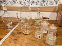 Group shot of all glass items on table: decanter, two pitchers, cruet, four jelly jars