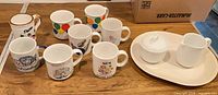 Group shot of platter, cream and sugar set, and eight mugs on table