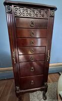 Front view of tall wooden jewelry armoire with closed drawers