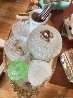Gold-tone mirrored tray holding multiple glass trinket jars and mug