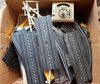 Box filled with assorted black straight and curved track pieces plus white supports and one controller visible