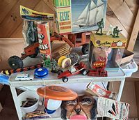 Overall view showing model kit, pick up stix, tractor, yo-yos, vehicles, Reagan puppet, mask and other toys on shelf