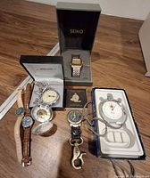 Group shot of all seven timepieces including boxed Seiko, boxed pocket watch, stopwatch, wristwatches, skeleton pocket watch, clip watch